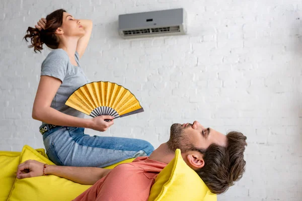 Young Woman Hand Fan Sitting Yellow Sofa Air Conditioner Lying — Stock Photo, Image