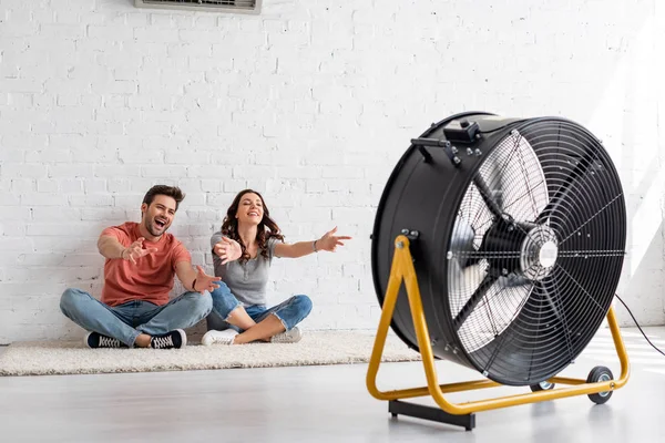 Animado Homem Mulher Sentado Chão Com Mãos Estendidas Frente Ventilador — Fotografia de Stock