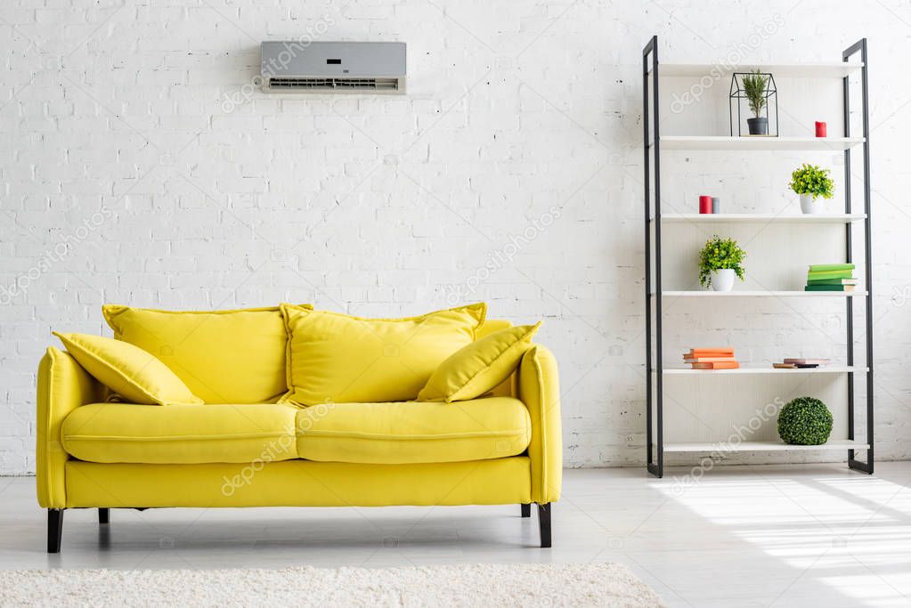 spacious living room with air conditioner on white wall, yellow sofa and rack 