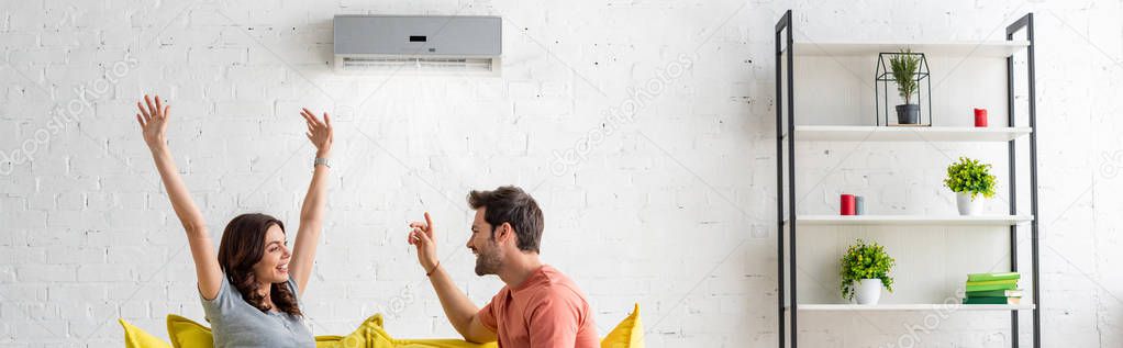 panoramic shot of excited man and woman sitting under air conditioner at home