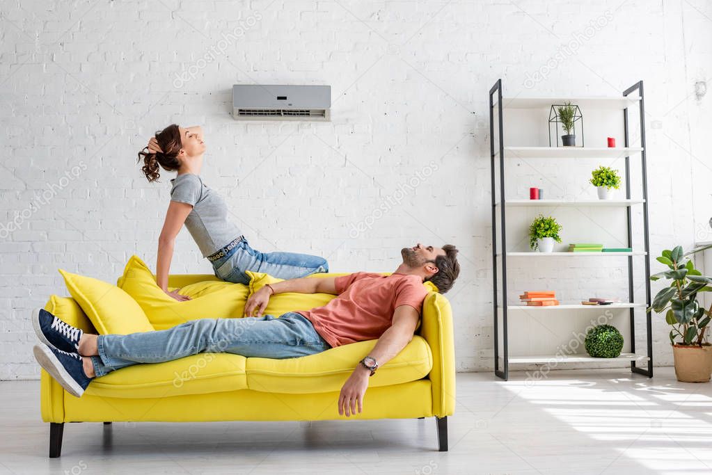 young man and woman resting on yellow sofa under air conditioner at home