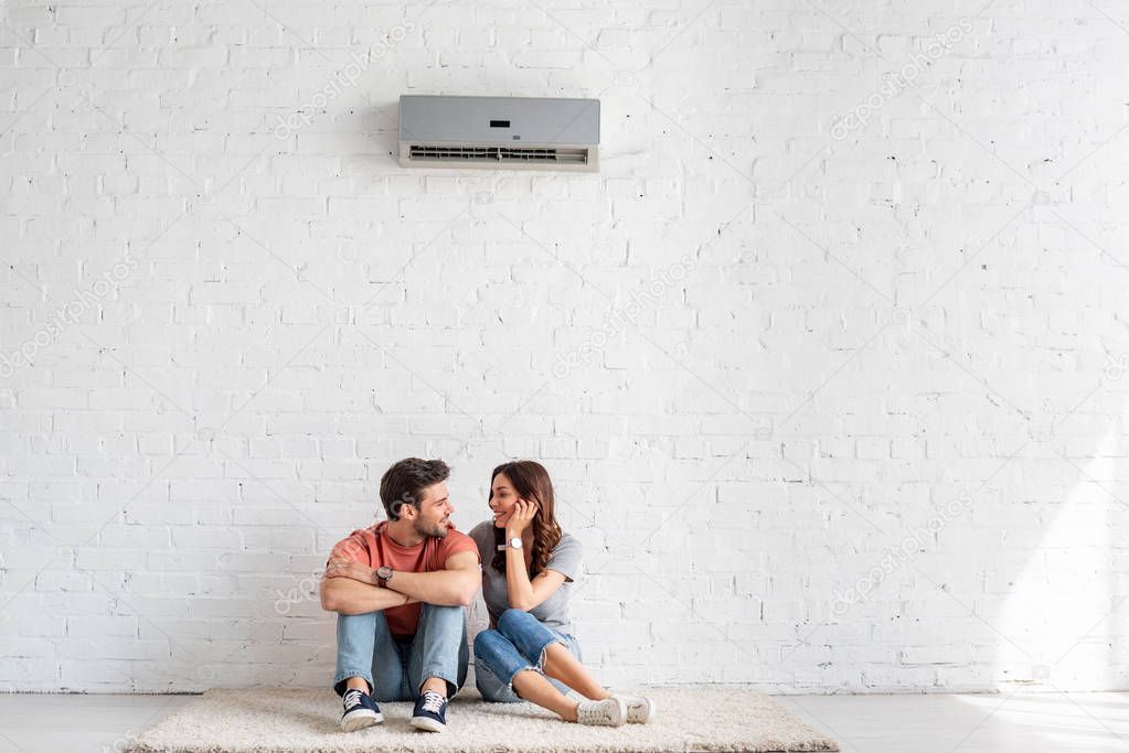 smiling couple talking while sitting on floor under air conditioner at home