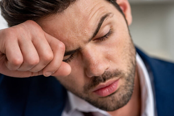 измученный красивый мужчина держит руку возле лица, страдая от жары на сером
