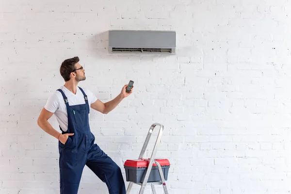 Workman Overalls Holding Remote Control While Standing Conditioner Stepladder Toolbox — Stock Photo, Image