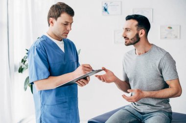 Hasta kanepede oturan ve Doktor klinik masaj kabine reçete yazma