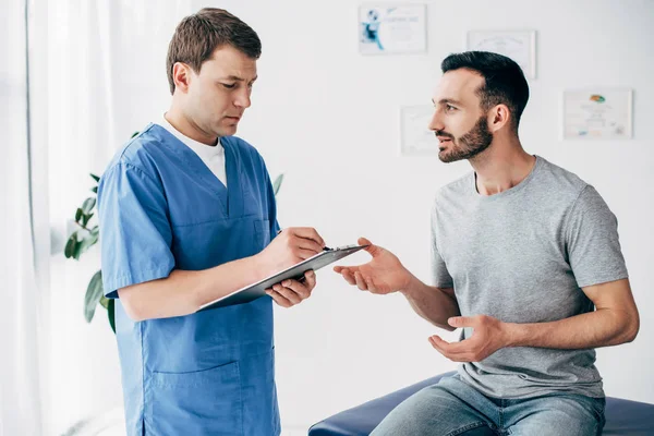 Hasta kanepede oturan ve Doktor klinik masaj kabine reçete yazma