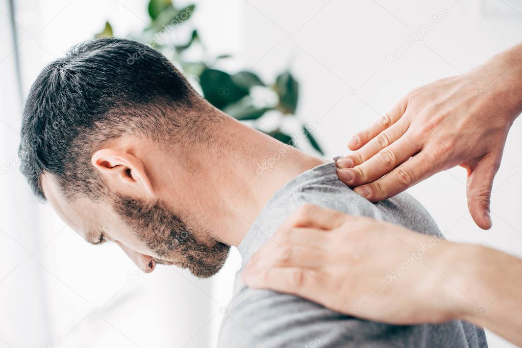 Cropped view of chiropractor massaging male patient neck in massage cabinet at clinic