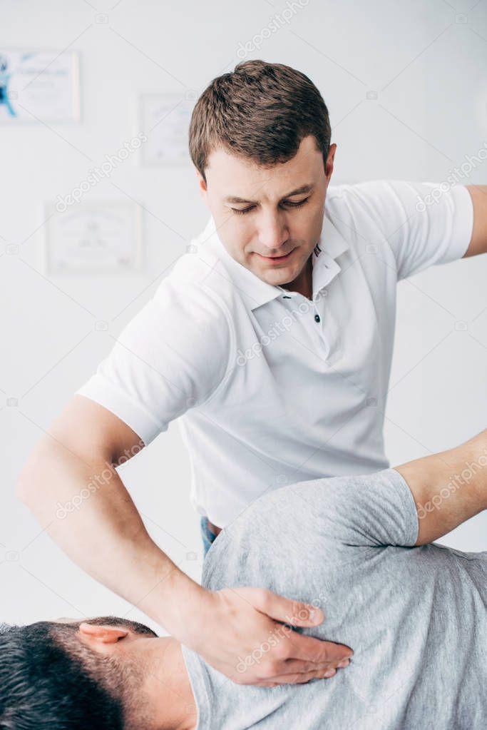 handsome chiropractor stretching arm of handsome patient in hospital