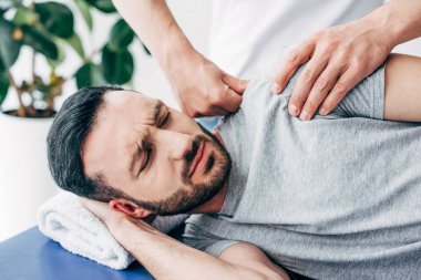 selective focus of chiropractor massaging shoulder of man in hospital clipart