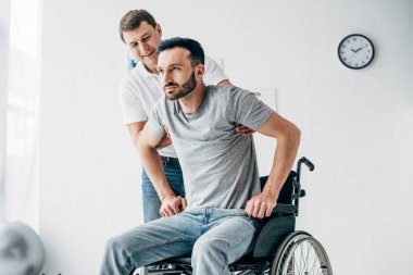 Hastanede iyileşme sırasında tekerlekli sandalyede özürlü adama yardım eden fizyoterapist