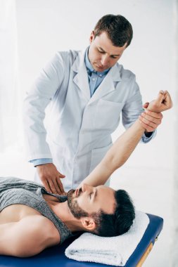 Hastane havlu ile masaj masasında yatan yakışıklı hastanın Kol germe chiropractor