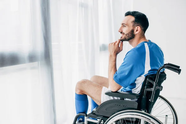 Sorrindo Homem Uniforme Futebol Sentado Cadeira Rodas Olhando Através Janela — Fotografia de Stock