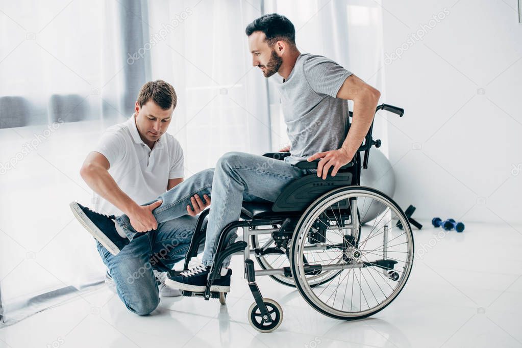 Physiotherapist massaging leg of handicapped man in wheelchair 