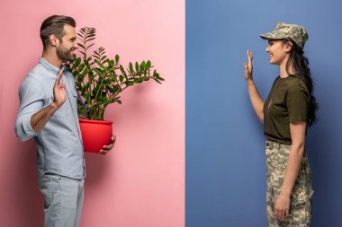 woman in military uniform waving at man with plant on blue and pink