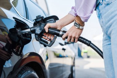 cropped view of woman holding fuel pump while refueling car with benzine  clipart