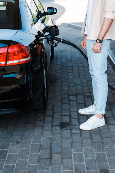 cropped view of man standing near black car at gas station 