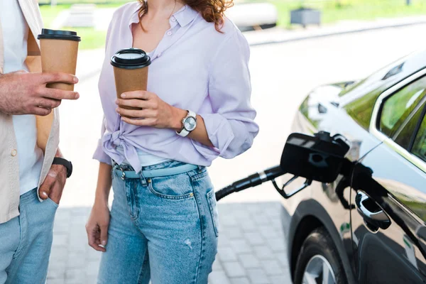 ガソリンスタンドで紙コップを持っている女性の近くにポケットに手を持って立っている男性のトリミングビュー — ストック写真