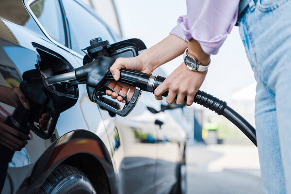 cropped view of woman holding fuel pump while refueling car with benzine 