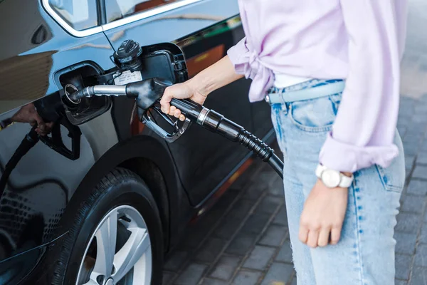 ベンジンで黒い車に燃料を補給しながら 燃料ポンプを保持している女性のトリミングビュー — ストック写真