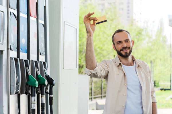 happy bearded man holding credit card and smiling at gas station 