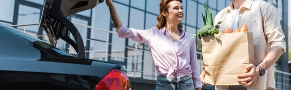 Panoramabild Lycklig Kvinna Tittar Man Innehar Papperskasse Nära Bil — Stockfoto