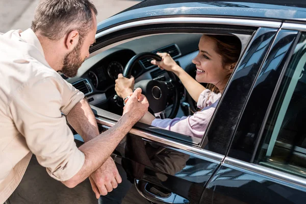 車の中でハンドルを握っている幸せな女性の近くに立っている男性の頭上の眺め — ストック写真