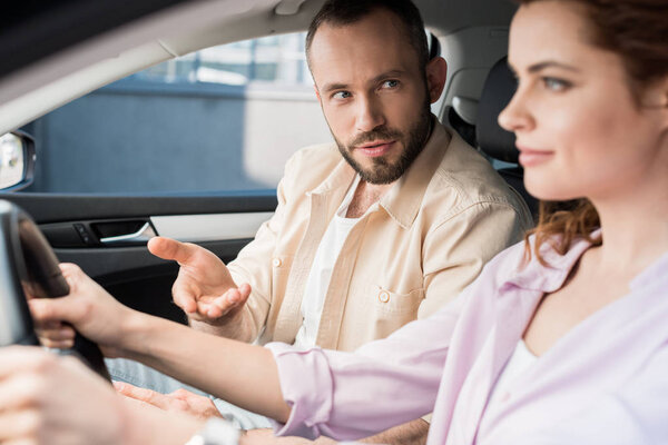 selective focus of handsome man gesturing near attractive woman driving car 