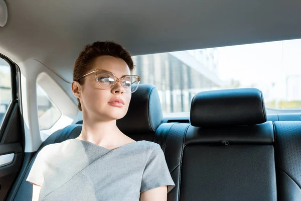 low angle view of attractive woman in glasses sitting in car