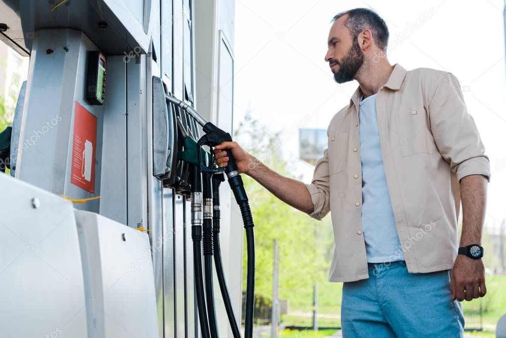 low angle view of man holding fuel nozzle at gas station 