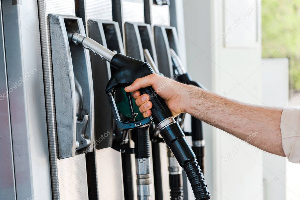 cropped view of man holding fuel nozzle at gas station 
