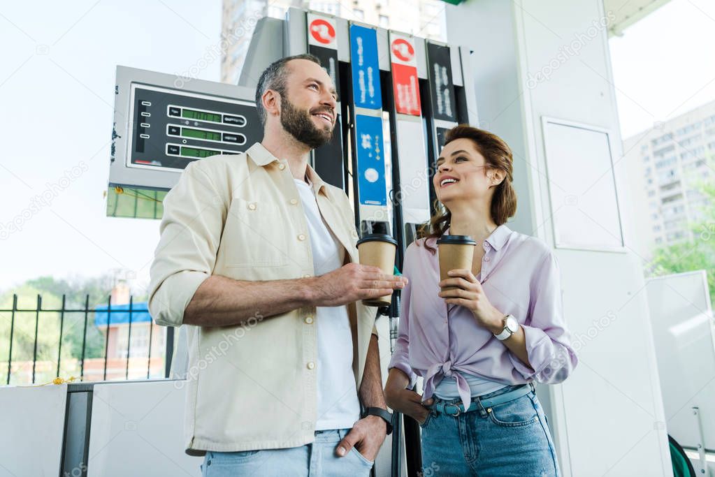low angle view of happy man and woman holding paper cups at gas station 