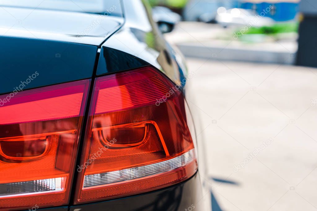 selective focus of red and shiny tail light of black and modern car 