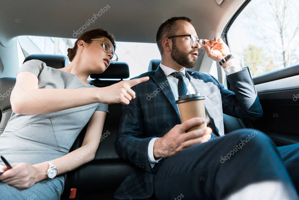 low angle view of businesswoman pointing with finger at window near surprised businessman in glasses  