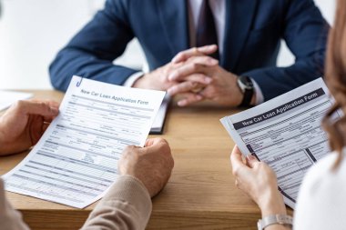 cropped view of customers holding contracts near car dealer with clenched hands clipart