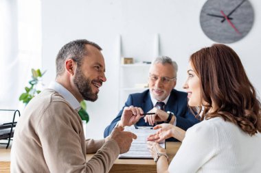 happy man looking at attractive woman while sitting near car dealer  clipart