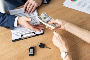 cropped view of woman giving dollar banknotes to car dealer in office  clipart
