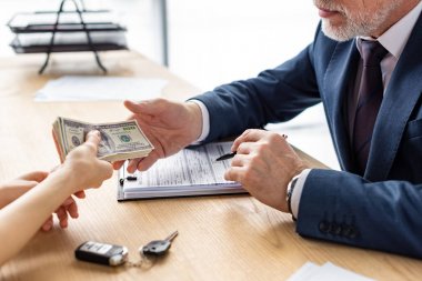 ofiste sakallı araba satıcısına dolar banknot veren kadının kırpılmış görünümü 