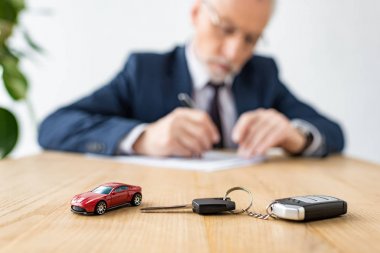 selective focus of toy car and car key near car dealer in office  clipart