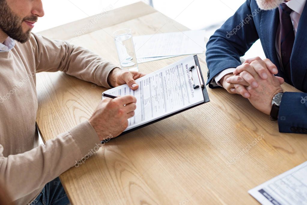 cropped view of man holding clipboard and signing agreement near car dealer 