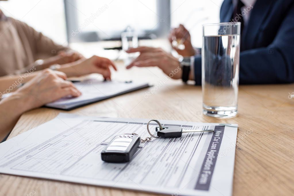 selective focus of car keys near agreement, glass of water, car dealer and customers 