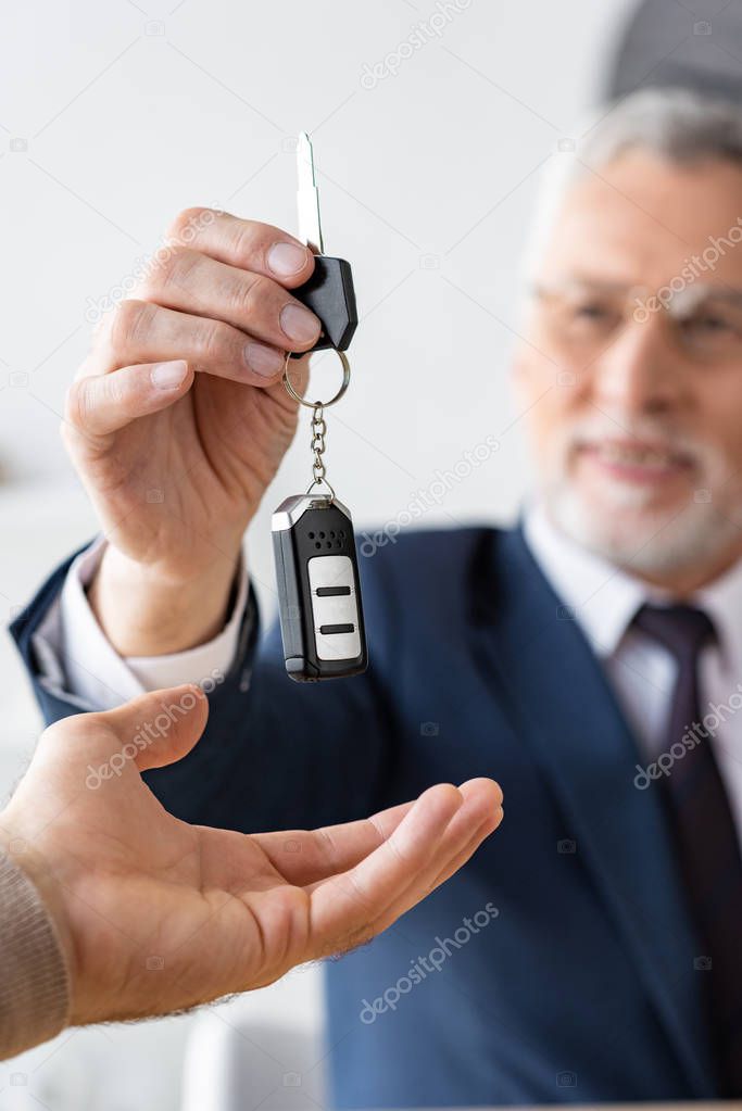 selective focus of car dealer in glasses giving car key to man in office 