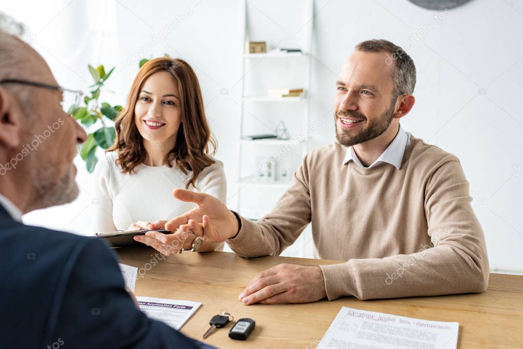 happy man gesturing near woman with clipboard and car dealer 