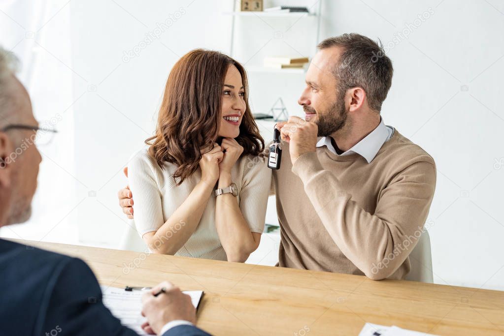selective focus of happy and attractive woman looking at man near car dealer 