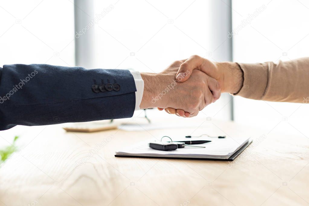 selective focus of man and car dealer shaking hands near clipboard, pen and car key 