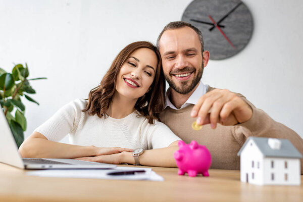 selective focus of happy man putting golden coin in pink piggy bank near attractive woman 
