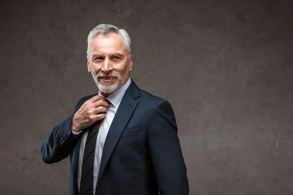 Vrolijke Bebaarde Zakenman Aanraken Stropdas Terwijl Glimlachend Grijs — Stockfoto