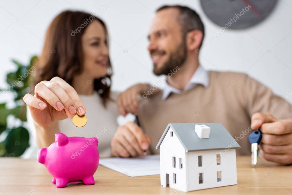 selective focus of happy woman putting golden coin in pink piggy bank near cheerful man 