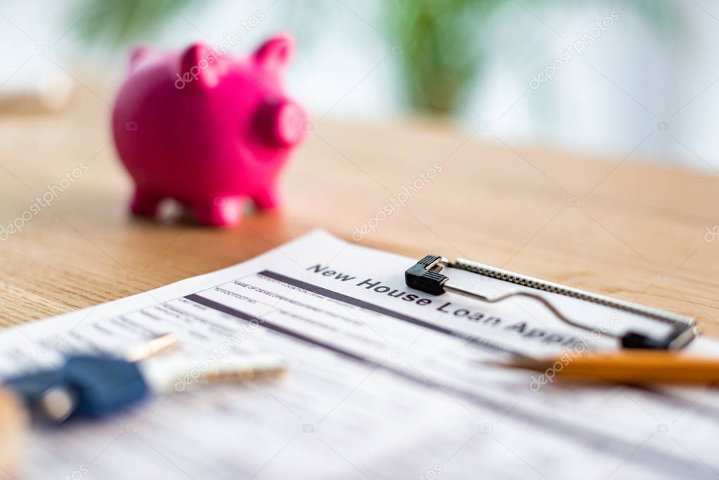 selective focus of clipboard with new house loan lettering on document near pencil, keys and pink piggy bank 