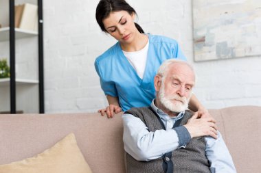 Doktor üzgün kıdemli adamın arkasında ayakta, omzuna el koyarak