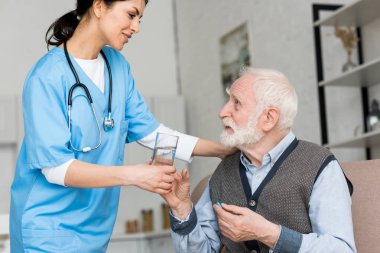 Nurse giving glass of water to elderly man with pill in hand clipart